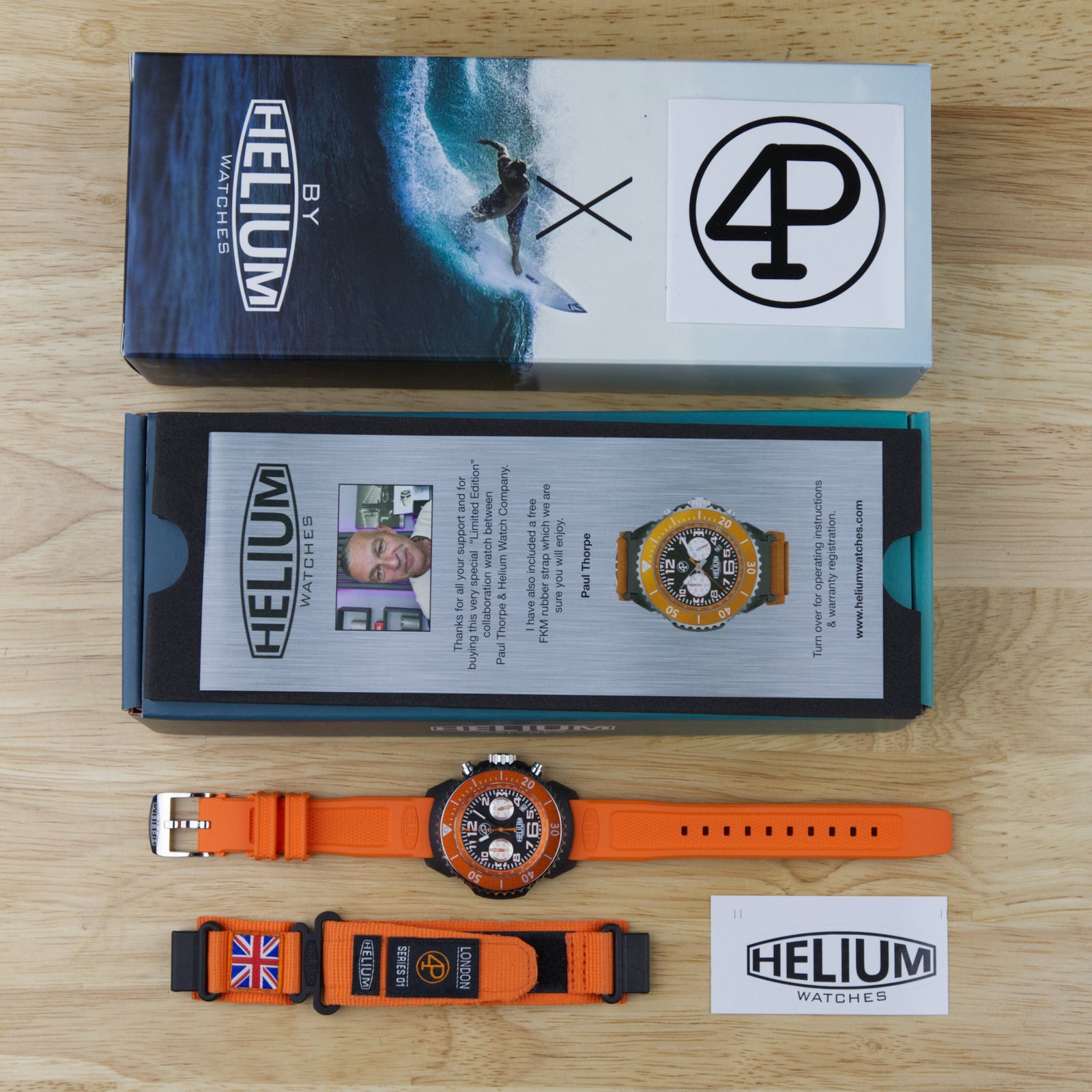 Orange watch with British flag strap next to Helium watch packaging on a wooden surface